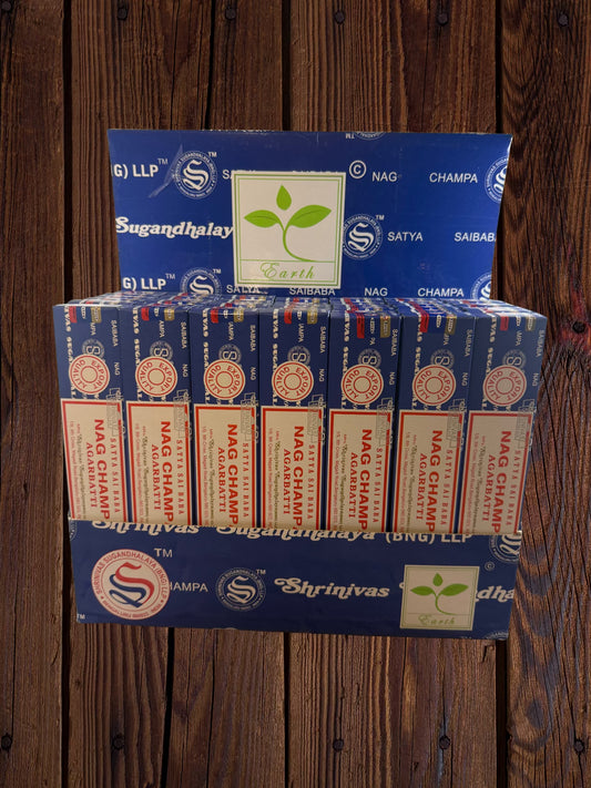 A display box filled with multiple packs of Nag Champa sticks, arranged on a wooden background. The packs are blue with white, red and gold text and logos, including Nag Champa, Shrinivas Sugandhalay.