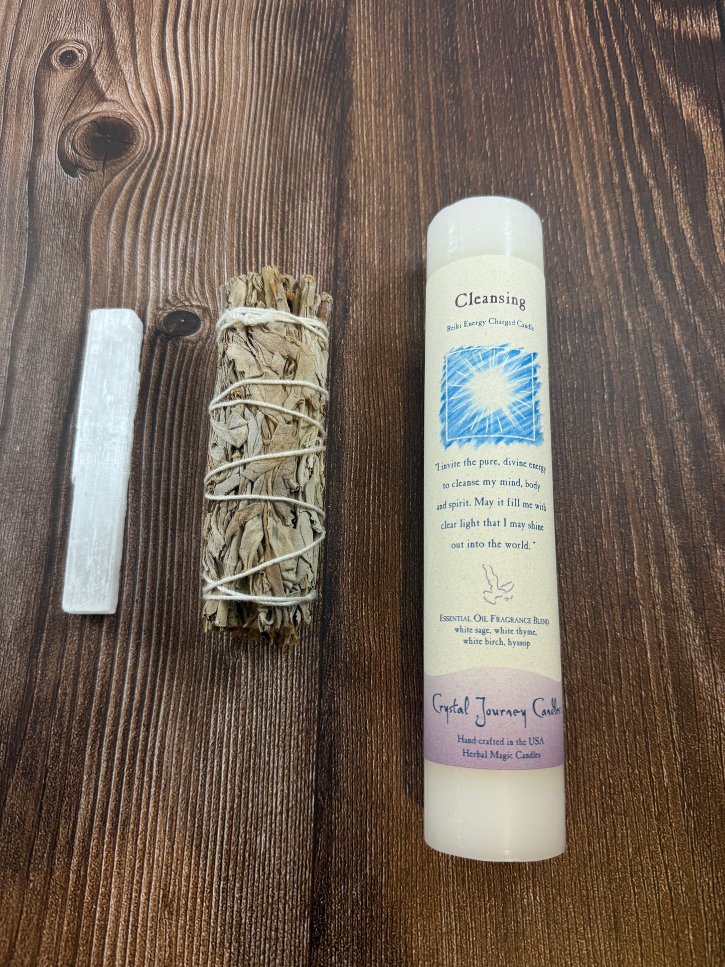 Overhead view of a selenite wand, white sage bundle and Crystal Journey cleansing pillar candle on wood