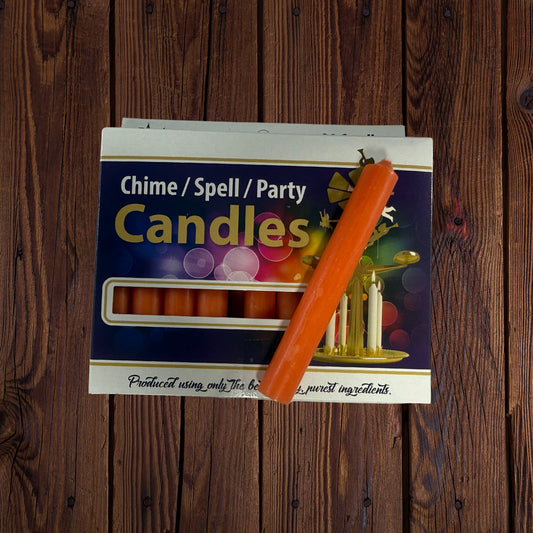 Candle across box: Orange chime candle resting diagonally across its box on a dark wooden surface
