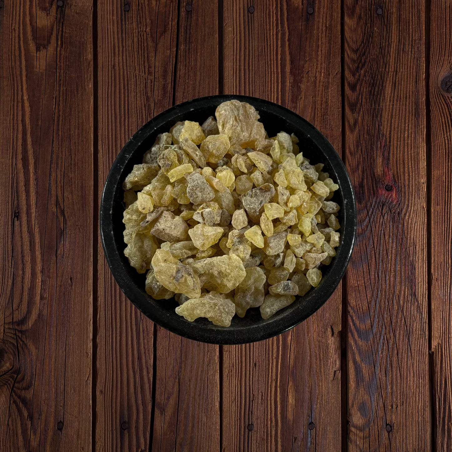 Peruvian golden copal resin pieces in a black bowl on a dark wooden surface.