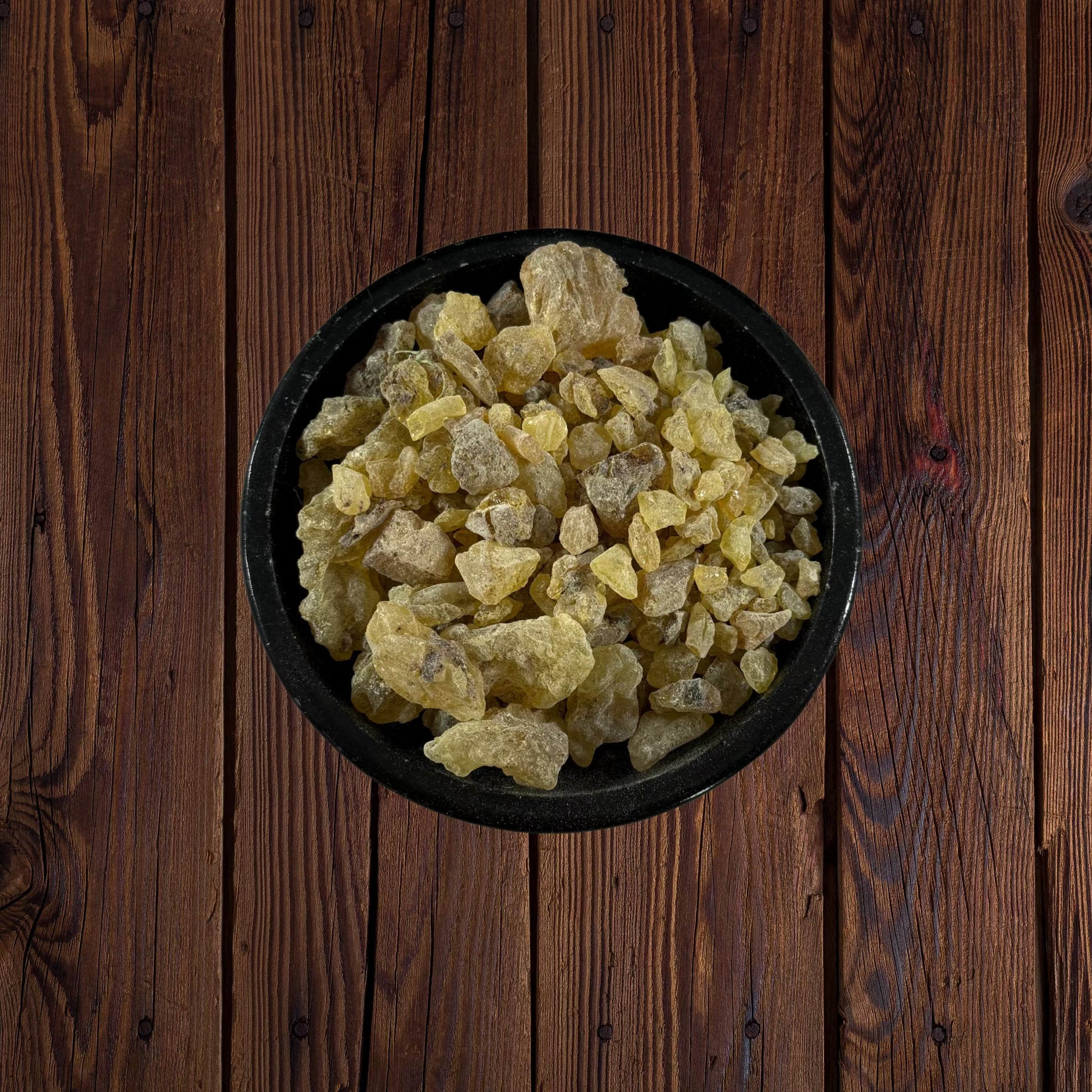 Peruvian golden copal resin pieces in a black bowl on a dark wooden surface.