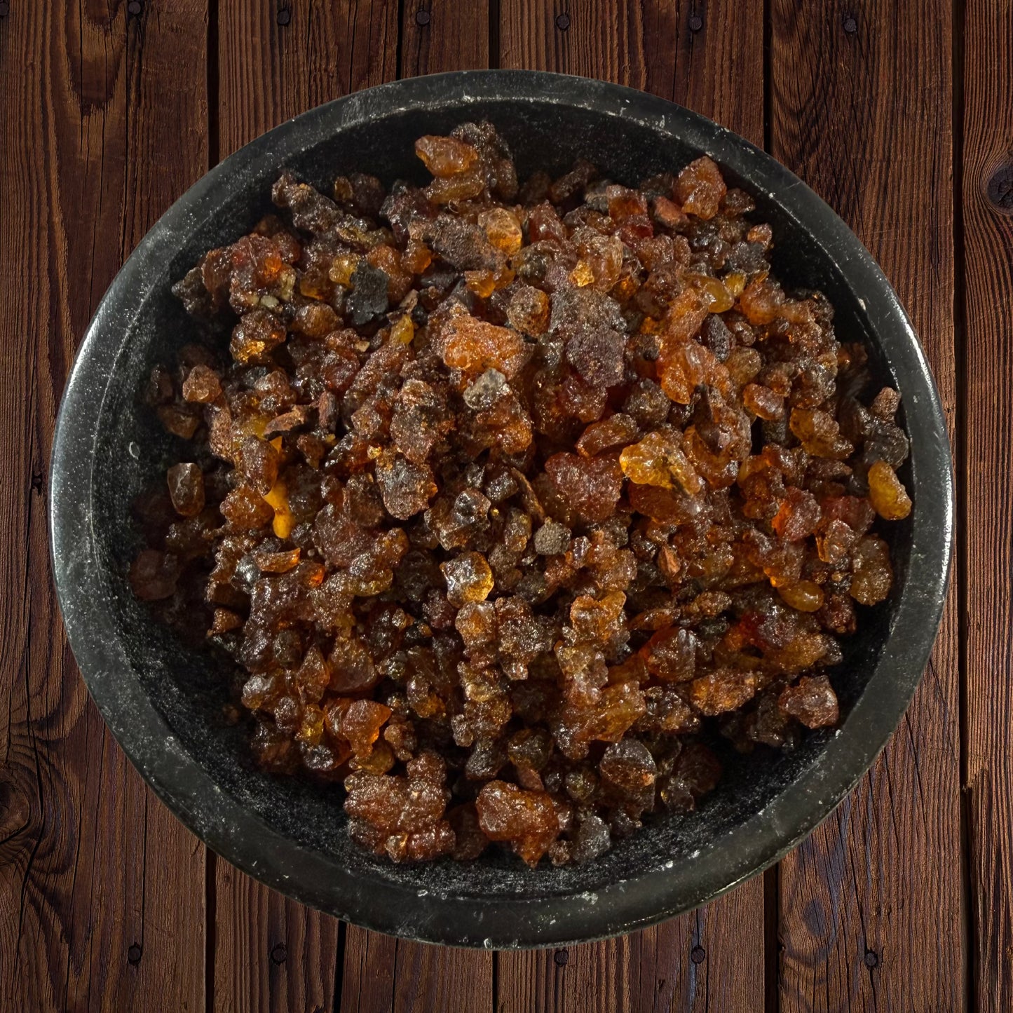 Myrrh resin incense pieces in a black bowl on a dark wooden surface.