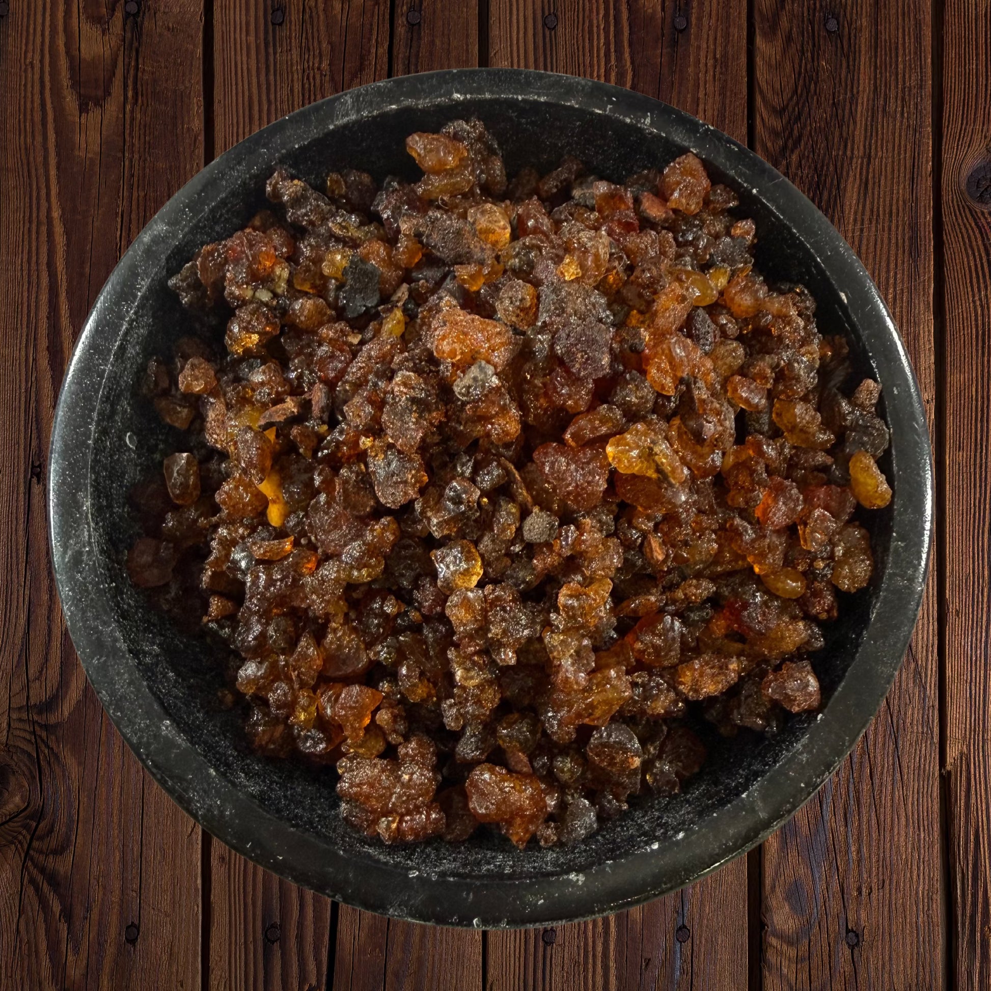 Myrrh resin incense pieces in a black bowl on a dark wooden surface.