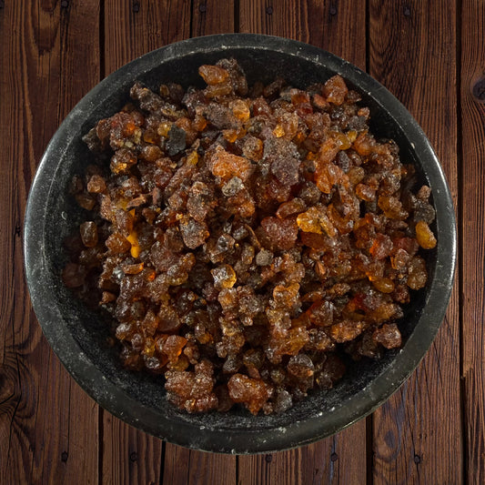 Myrrh resin incense pieces in a black bowl on a dark wooden surface.