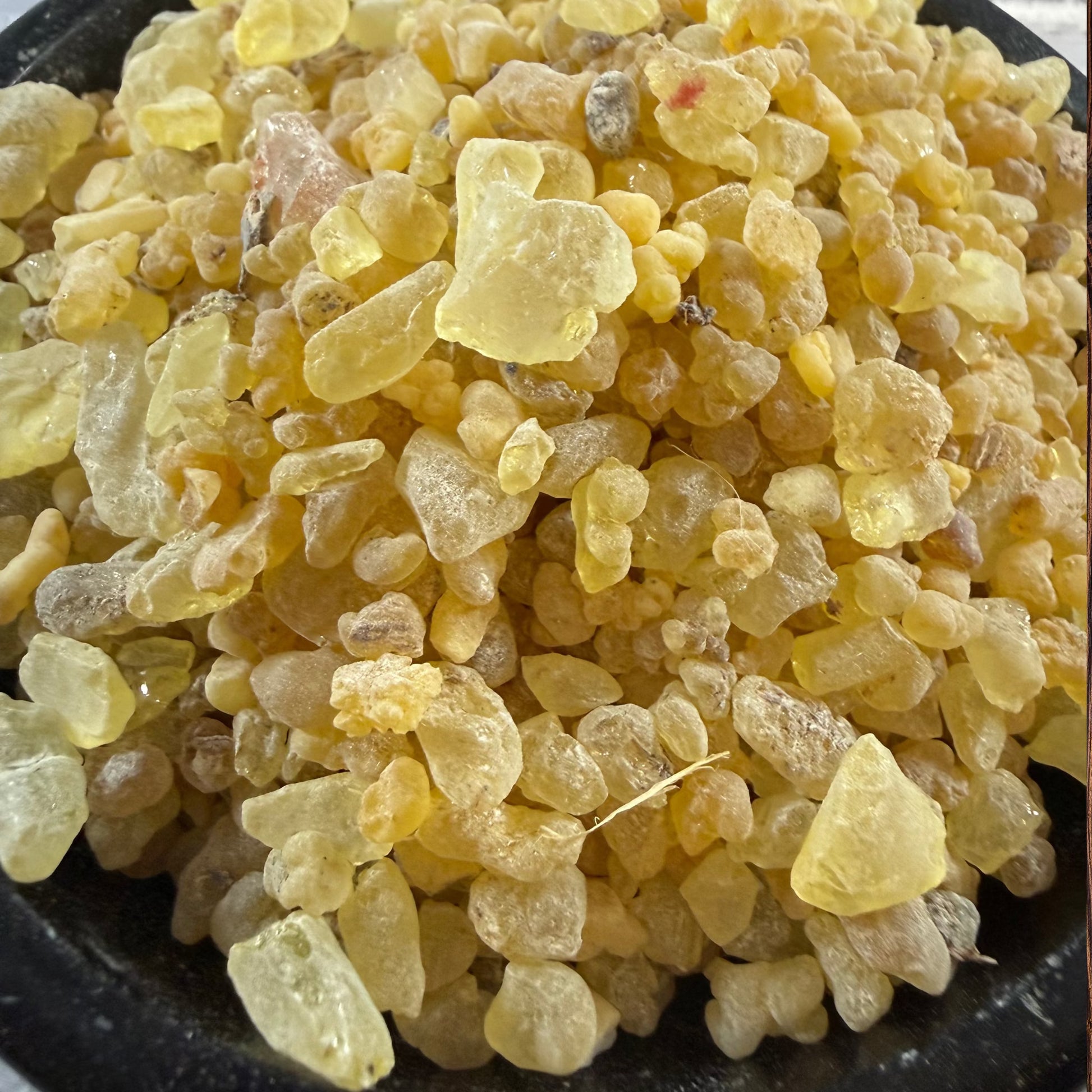 Close-up of pale yellow Altar Blend resin pieces piled in a black bowl