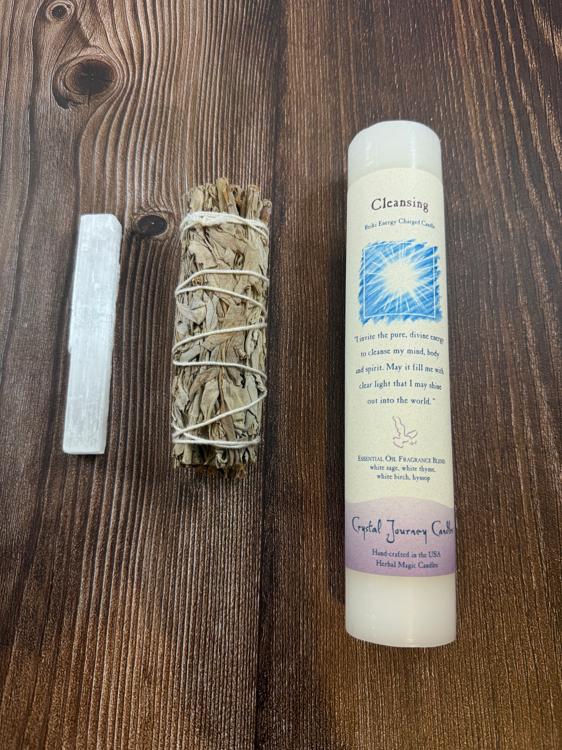 Black gift bag with moon-patterned tissue, selenite wand, white sage bundle and cleansing pillar candle arranged on wood